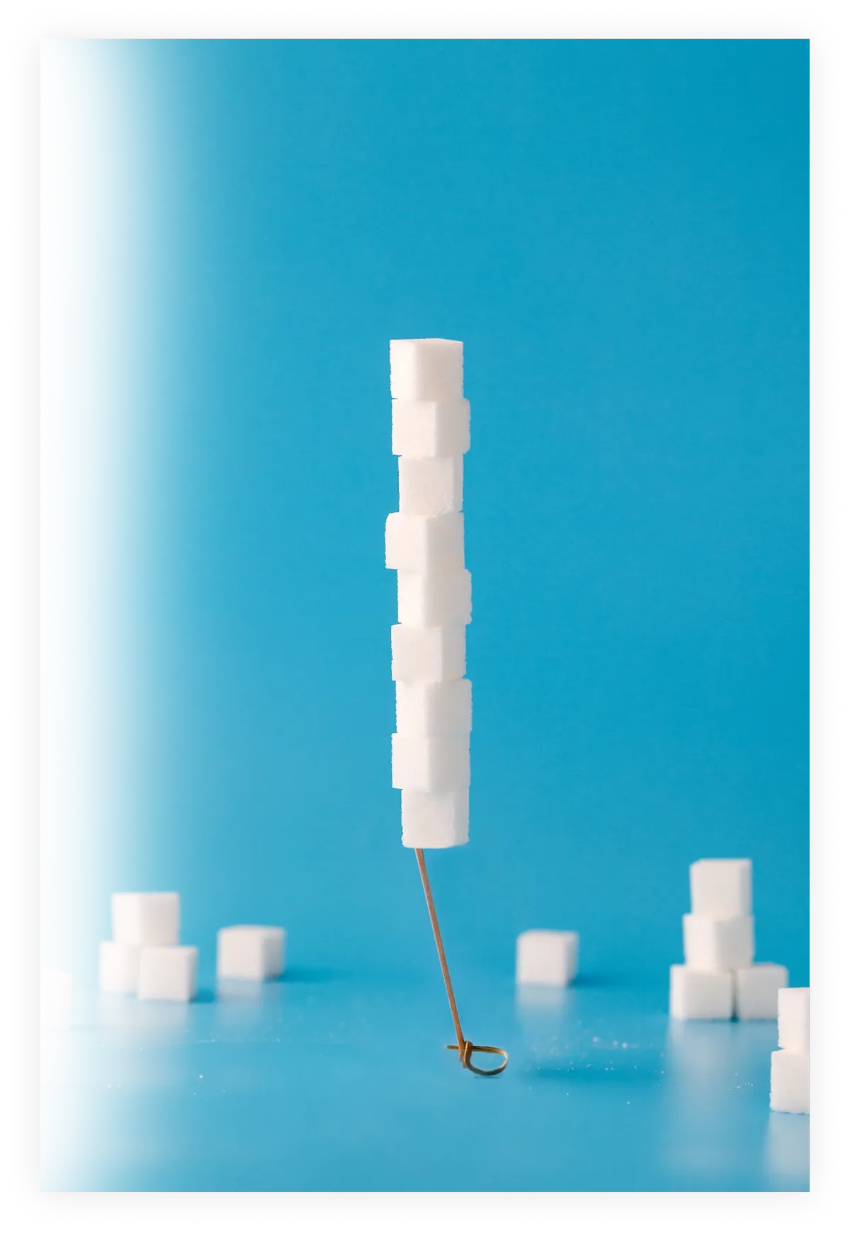 Πύργος από λευκούς κύβους ζάχαρης με σύριγγα σε γαλάζιο φόντο που συμβολίζει τον έλεγχο γλυκόζης και τον διαβήτη